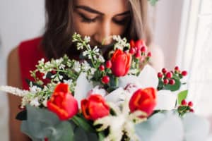 Beautiful bouquet of red and white winter flowers with greenery. Young woman admiring and smelling the flowers.